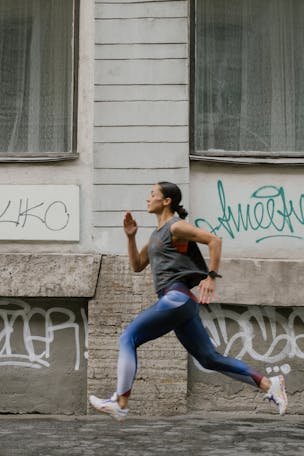 A woman in activewear jogging swiftly past a graffitied wall in an urban setting.