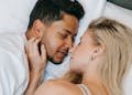 A loving couple, man and woman, resting closely together on a bed indoors during the daytime.