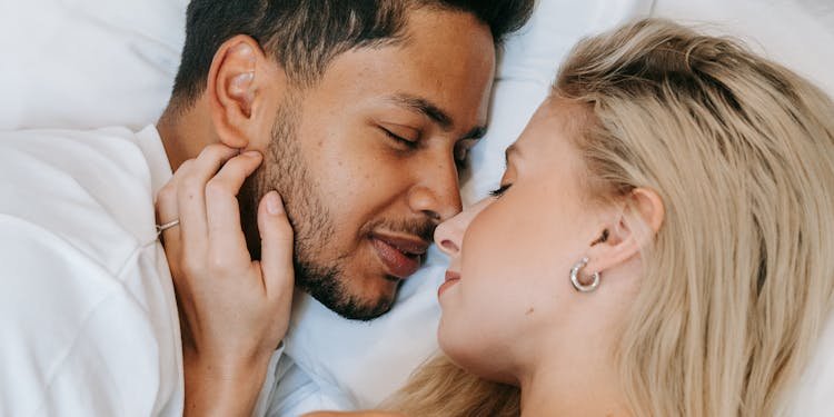 A loving couple, man and woman, resting closely together on a bed indoors during the daytime.