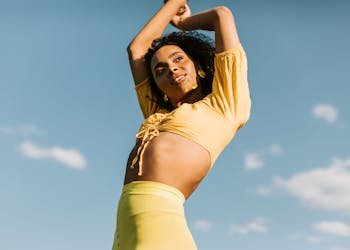 Charming woman with curly hair poses confidently against a clear blue sky, exuding joy and energy.